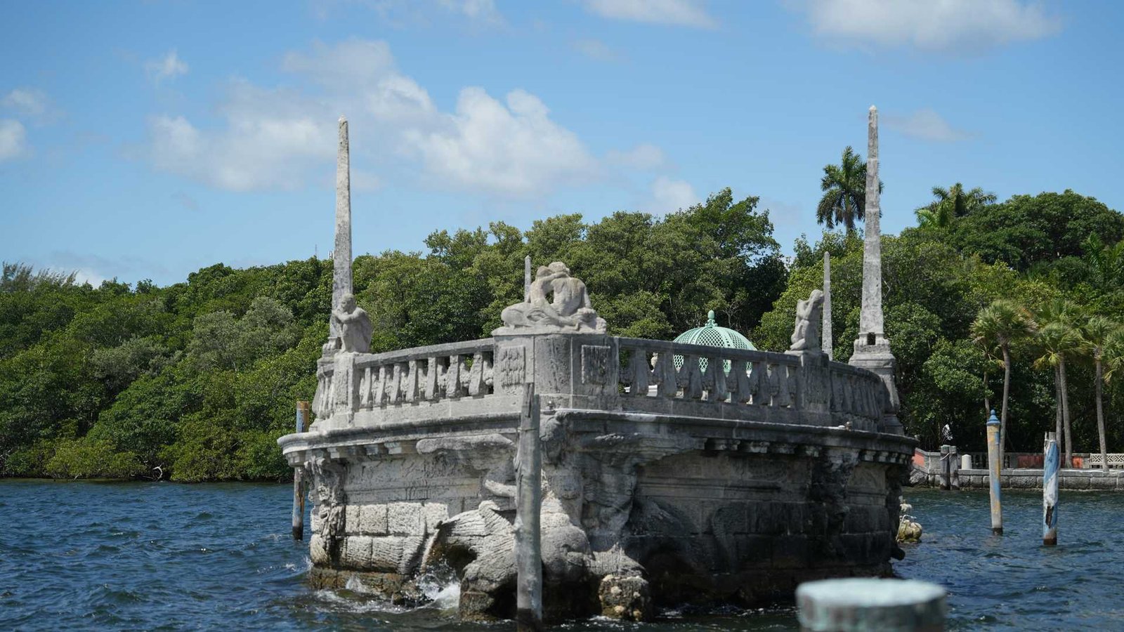 La icónica barcaza de piedra caliza esculpida frente a la bahía de Biscayne en la Villa Vizcaya, rodeada de aguas turquesa al atardecer.